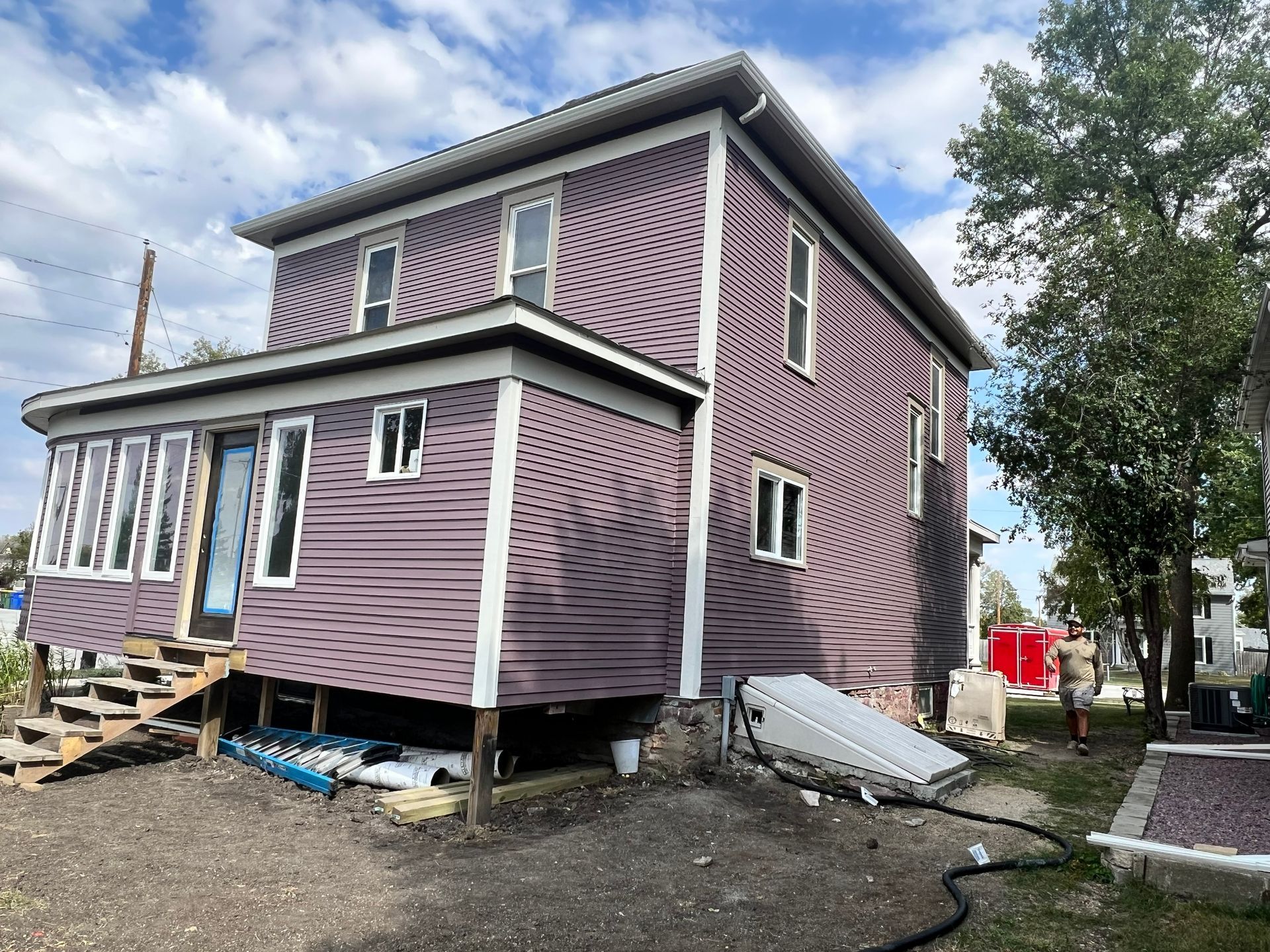 Two-story house with purple siding, white trim, and a porch under construction.