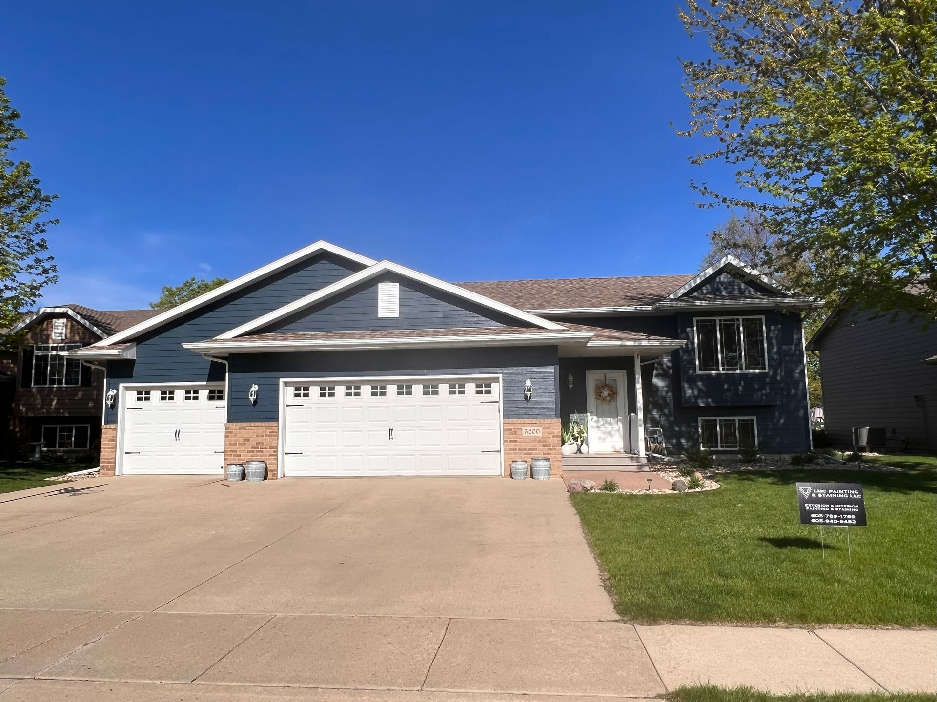 Blue house with white trim and garage doors, concrete driveway, and green lawn.