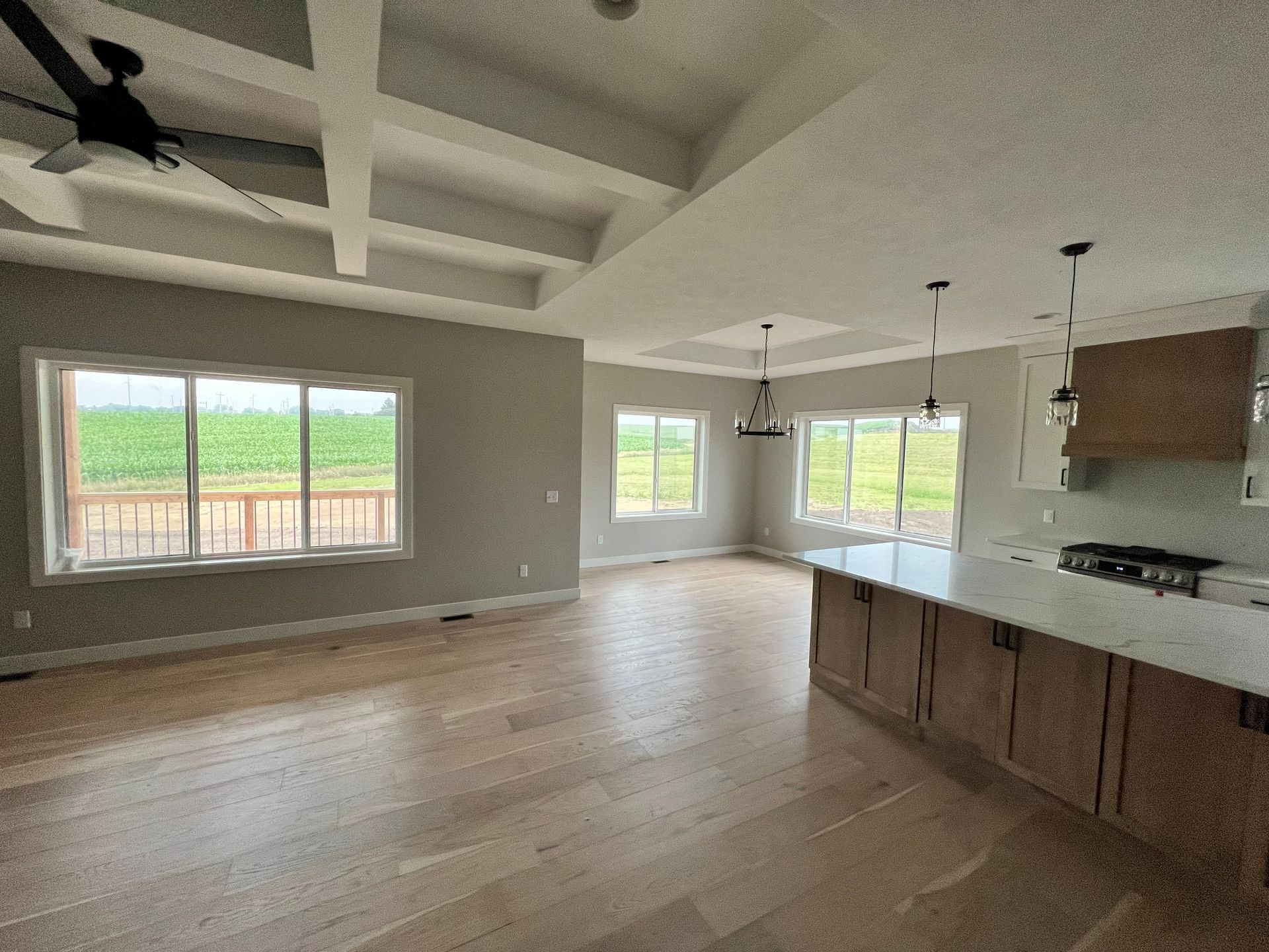 Spacious, light-filled interior with hardwood floors, a kitchen island, and large windows overlooking a green field.
