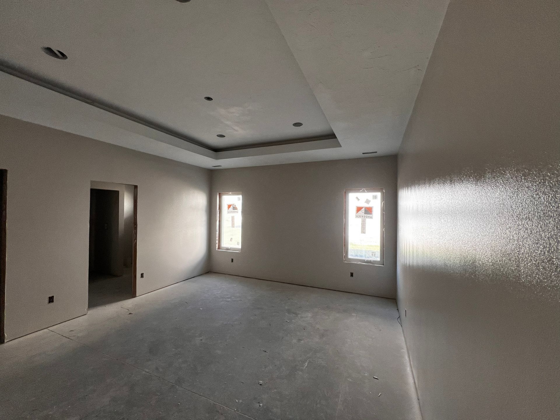 Empty room with gray walls, two windows, and recessed ceiling lighting, under construction.