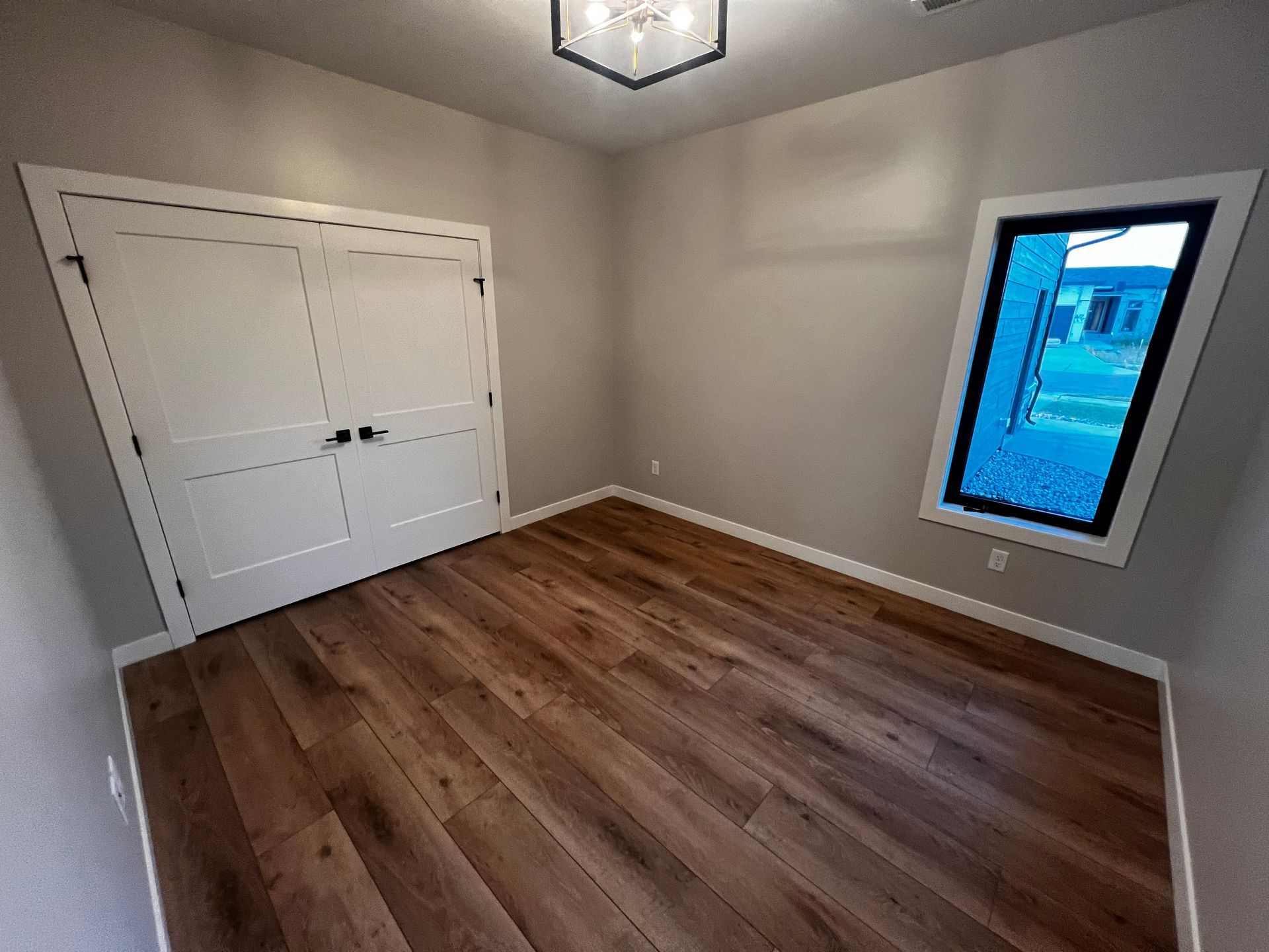 Empty room with hardwood floors, white doors, a window, and a modern light fixture.