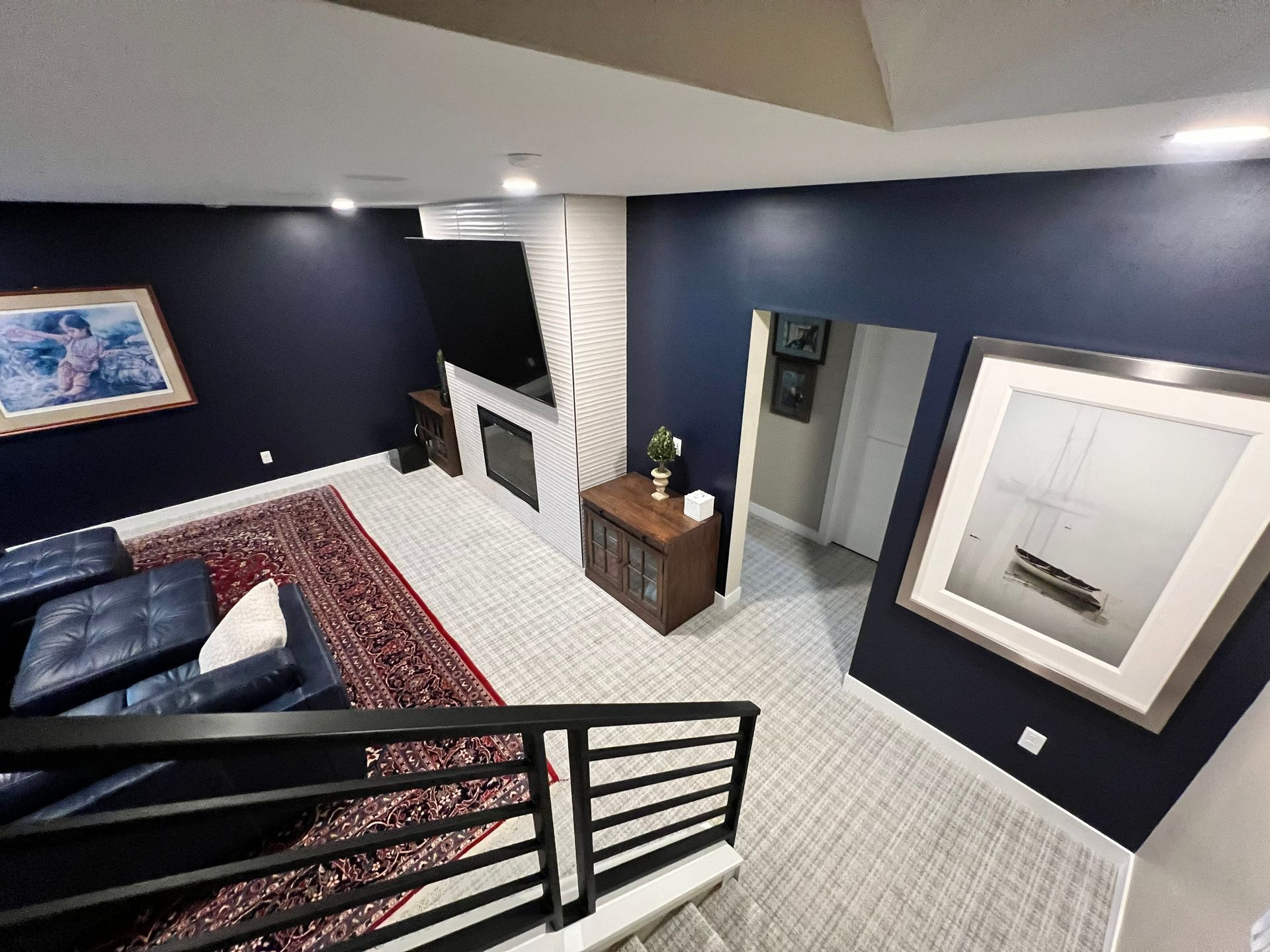 A navy blue room with a rug, sofa, fireplace, and staircase leading down.