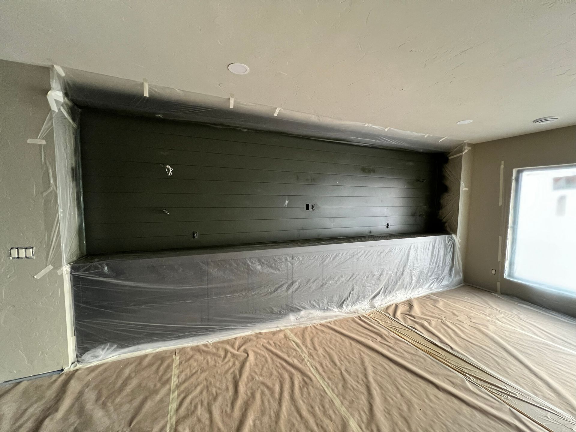 Room with a green accent wall. Plastic sheeting covers the floor and lower wall sections, protecting surfaces during construction.
