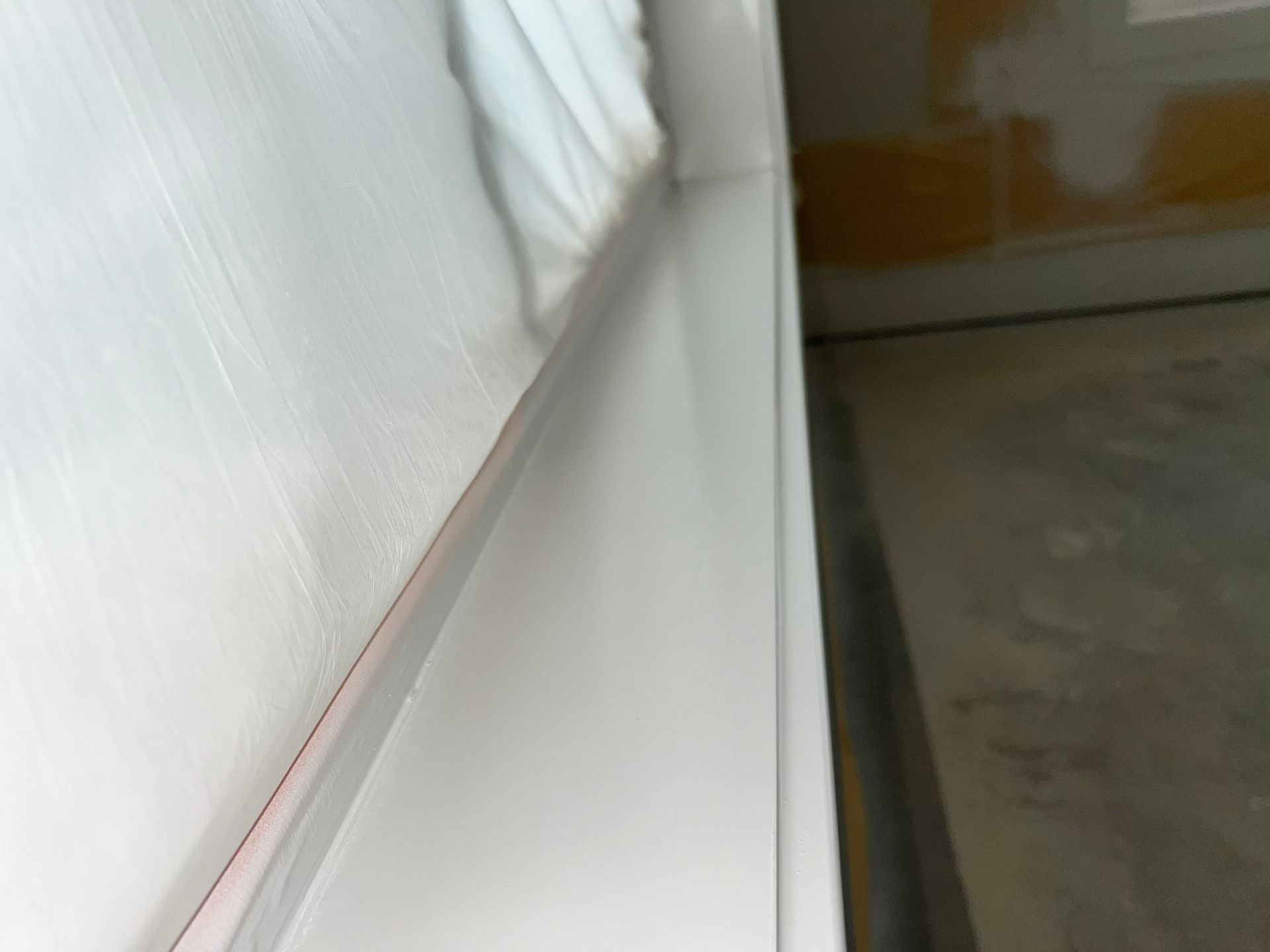 White painted windowsill and wall partially covered in plastic sheeting, next to a bare wall.
