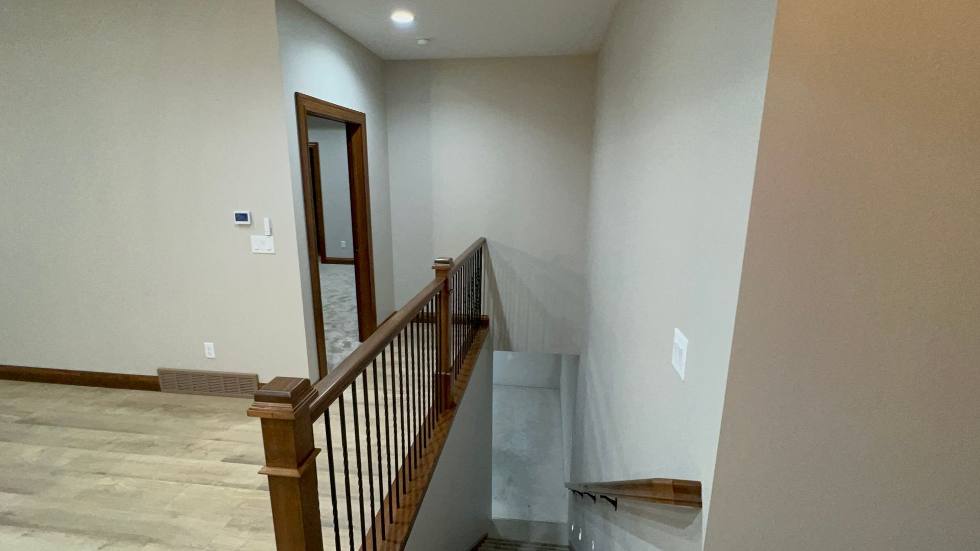 Hallway with wooden staircase leading down, light beige walls, hardwood floors.