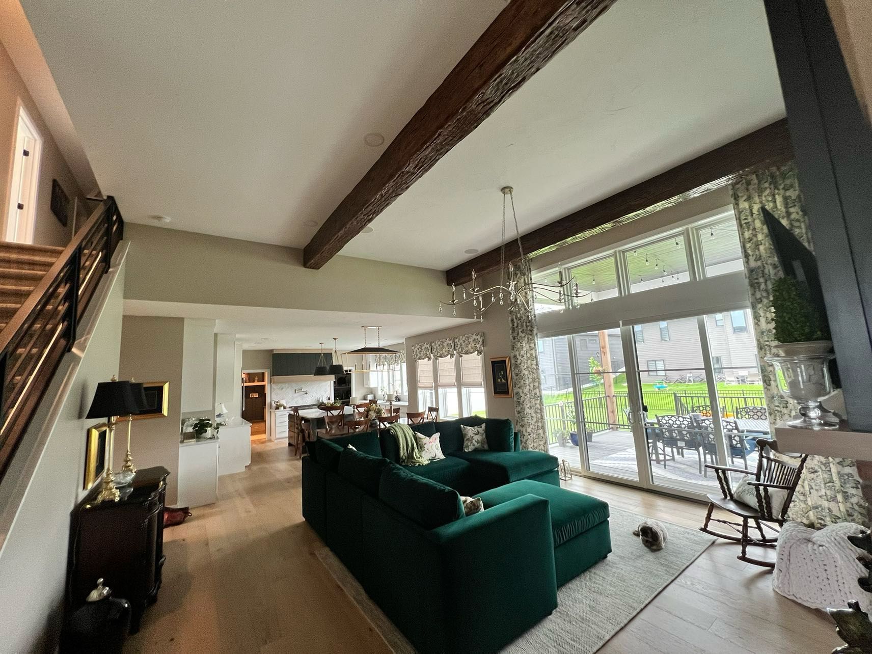 Spacious living room with a green sectional, wooden beams, and a large window overlooking a patio.
