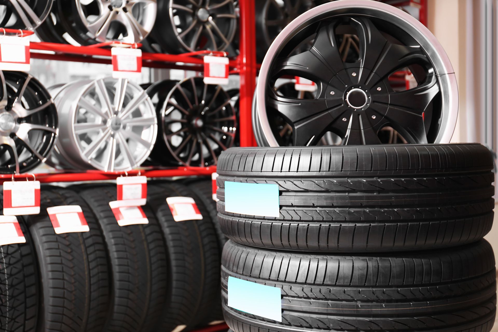 Tires and rims stacked in a store, red shelving. Black tires and black and silver rims are visible.