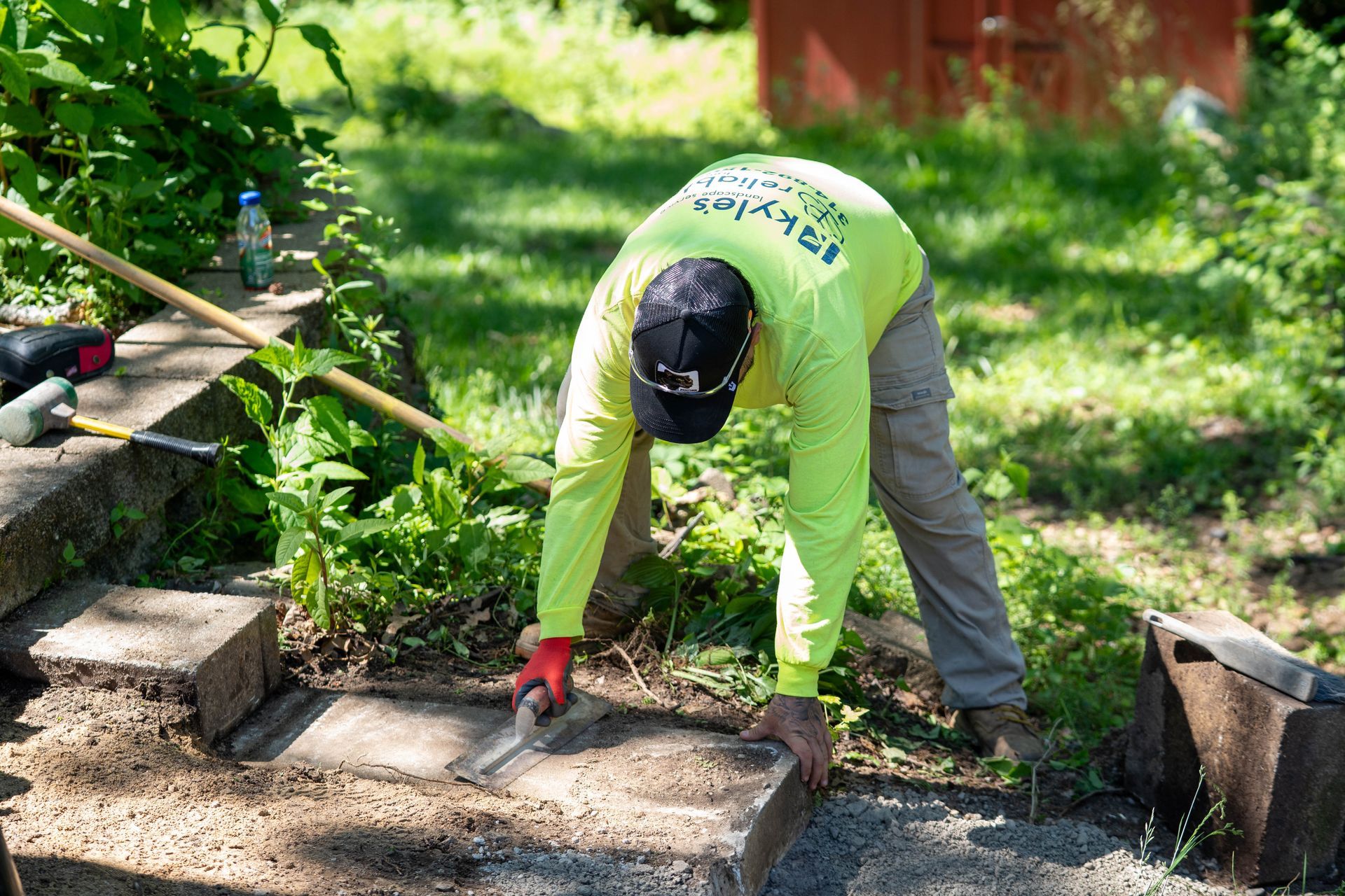 Person in a neon green shirt and cap uses a trowel to work on stone steps outdoors.