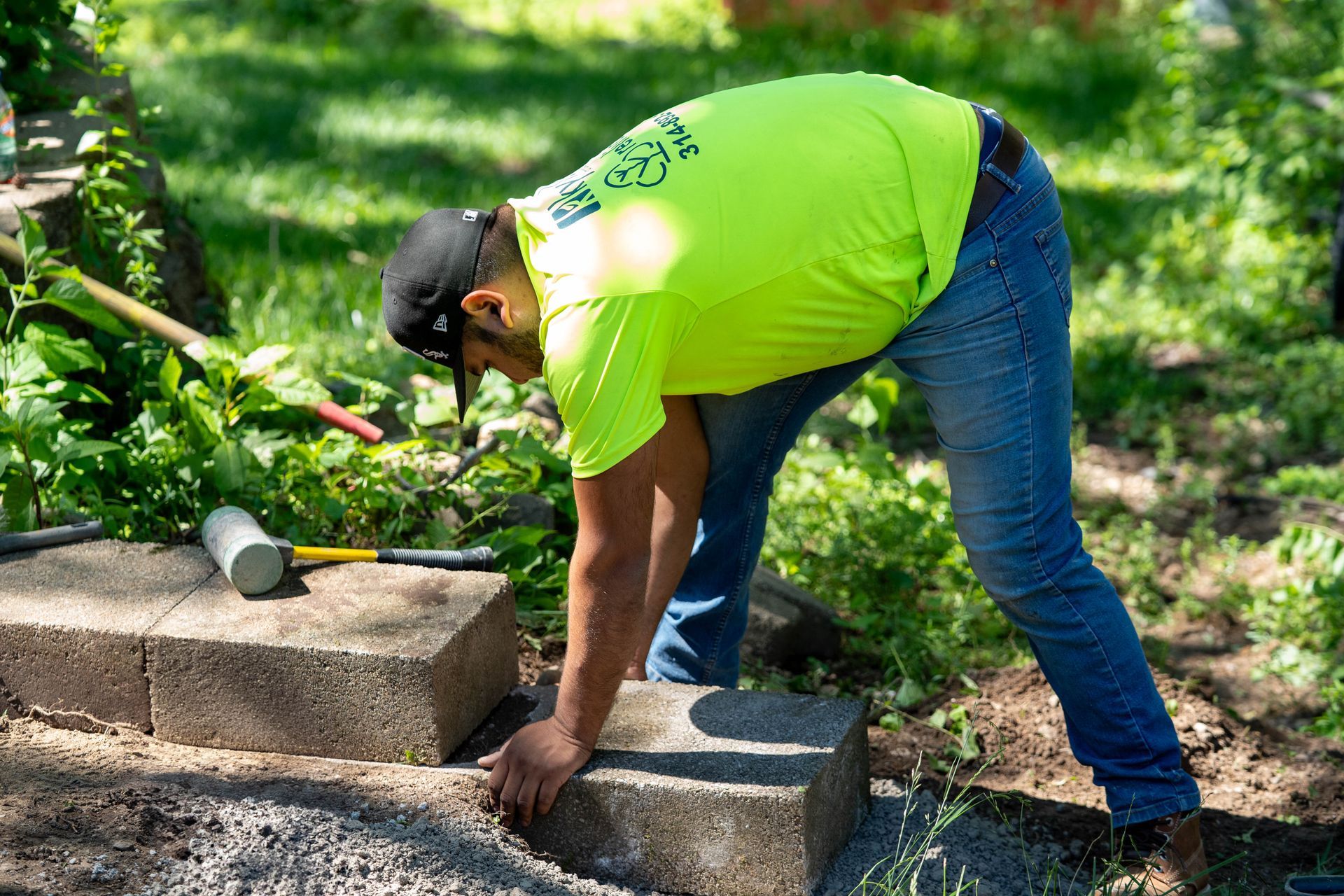 Man in neon shirt laying brick pavers outdoors.