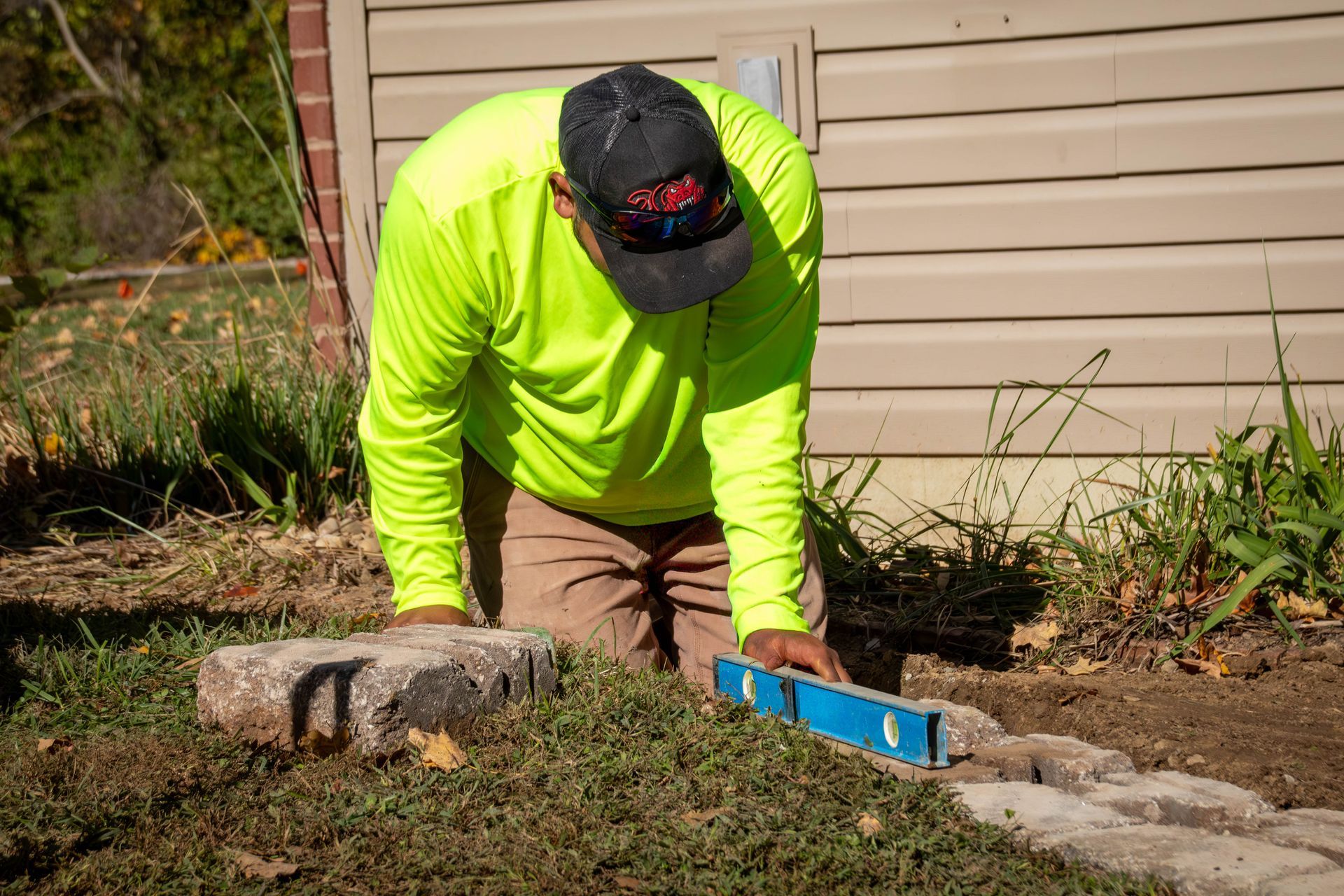 Person in neon shirt using a level to lay stones outdoors.
