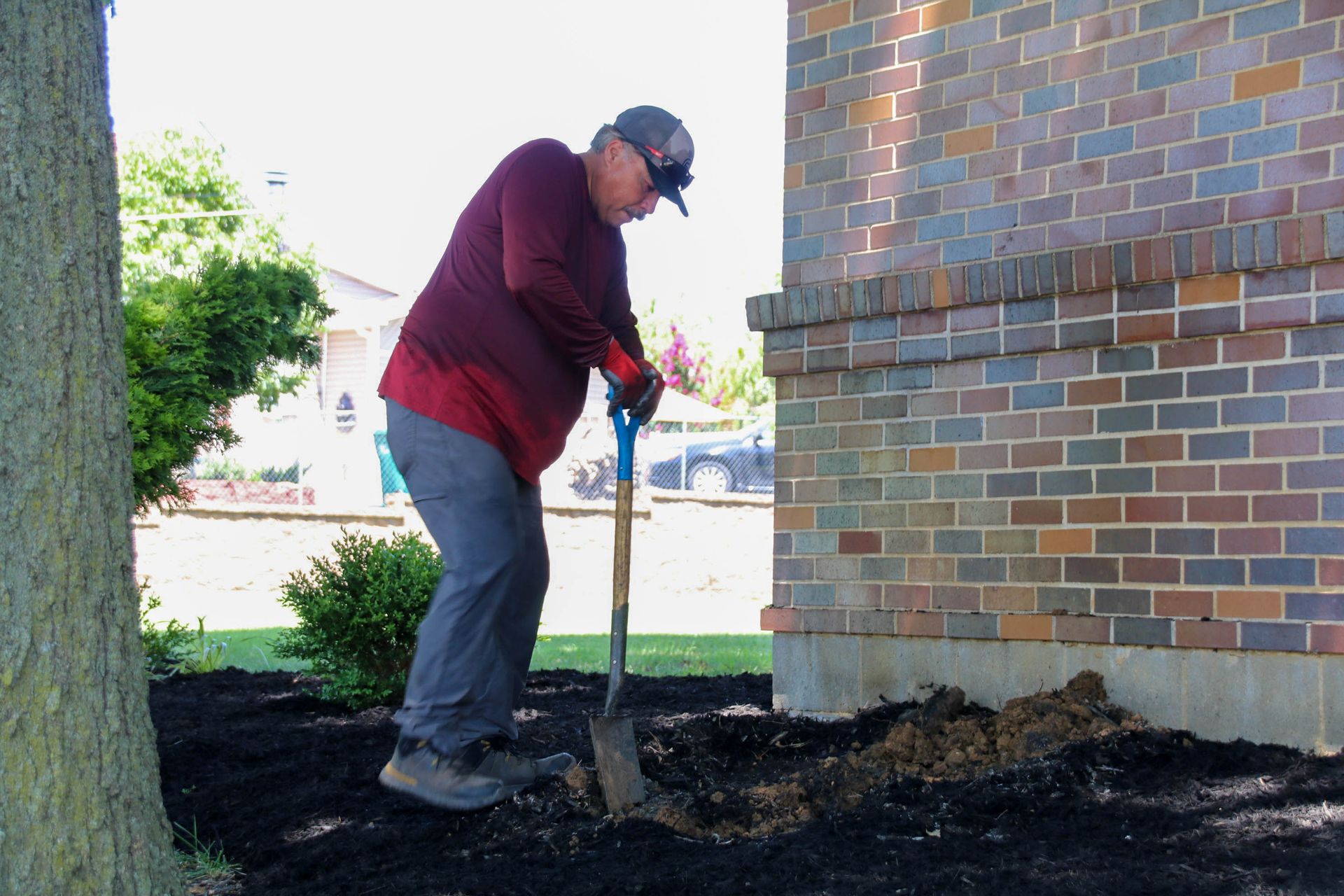 Man using a shovel to dig in a garden bed next to a brick building.