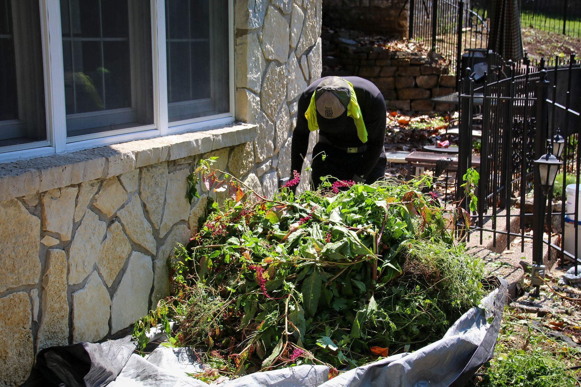Person raking yard waste into tarp near a stone-faced building.