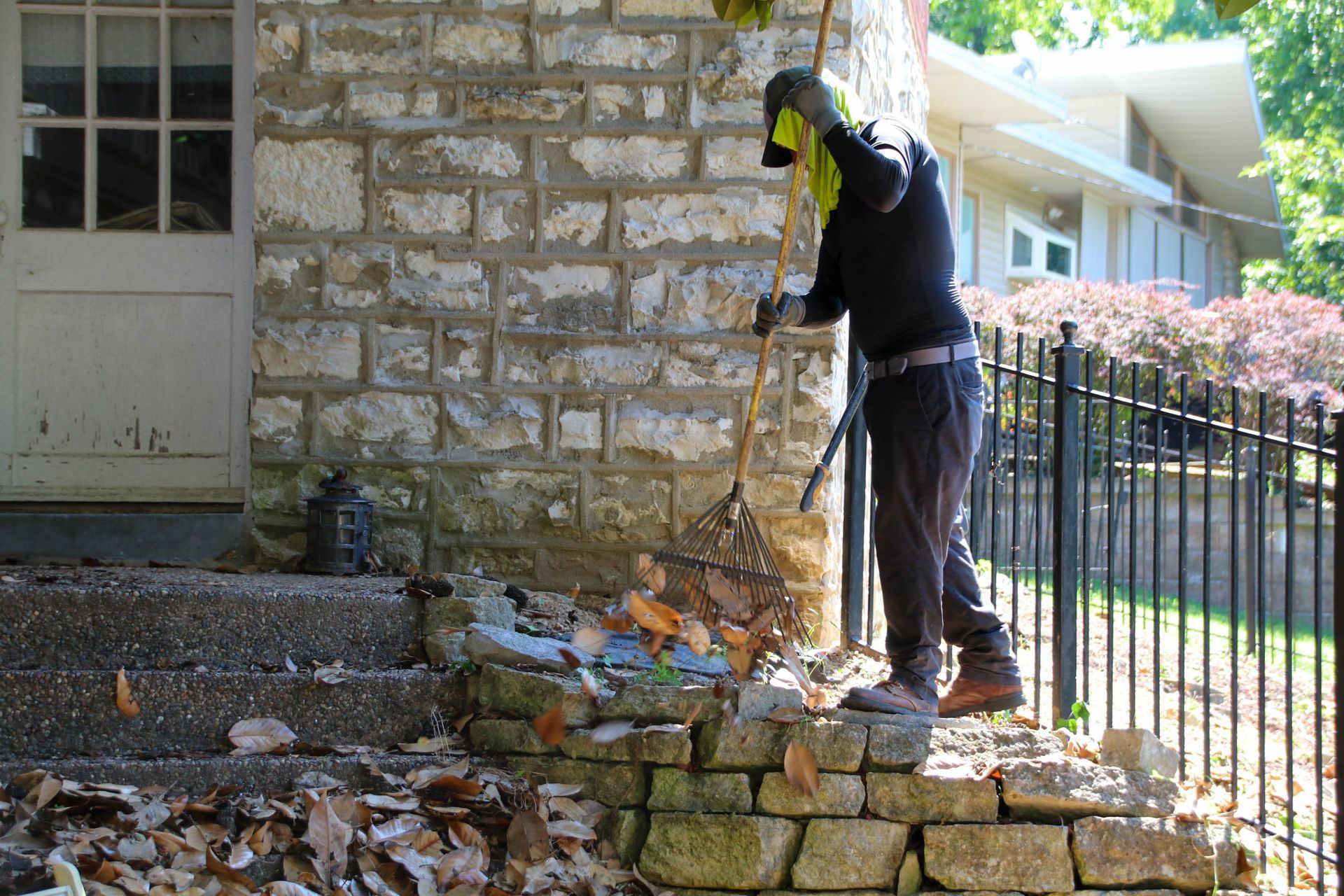 Person rakes leaves near stone wall and steps, next to a door.