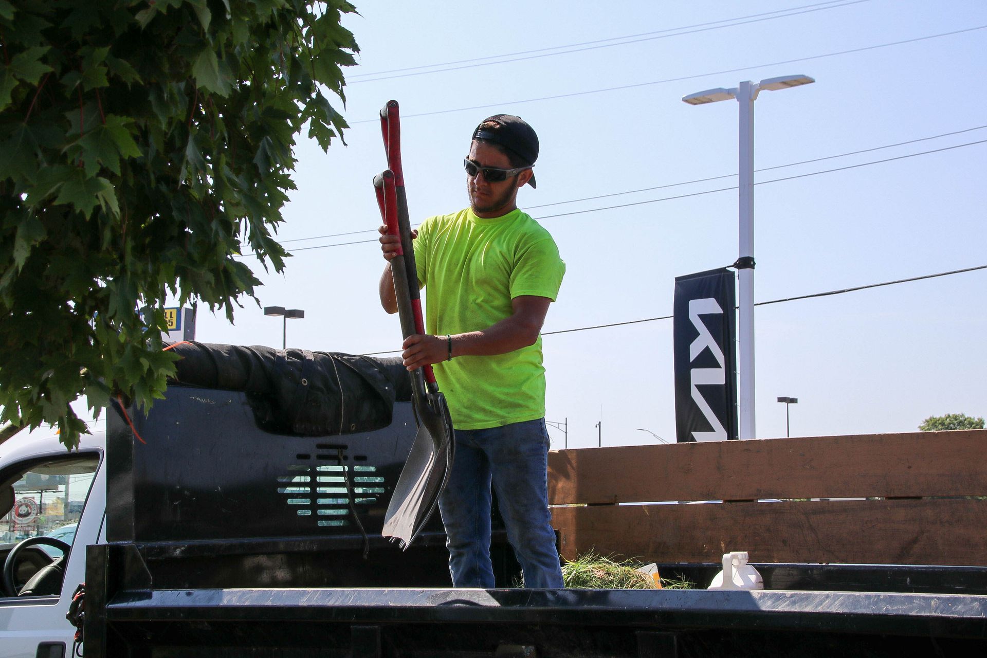 Person holding a red shovel in a truck bed, near a KIA dealership.