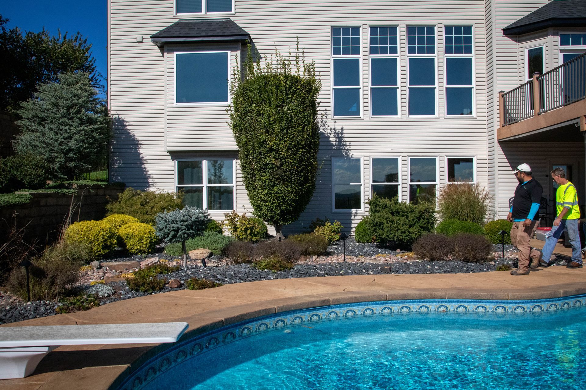 Two men near a pool, a house with windows, and landscaping.