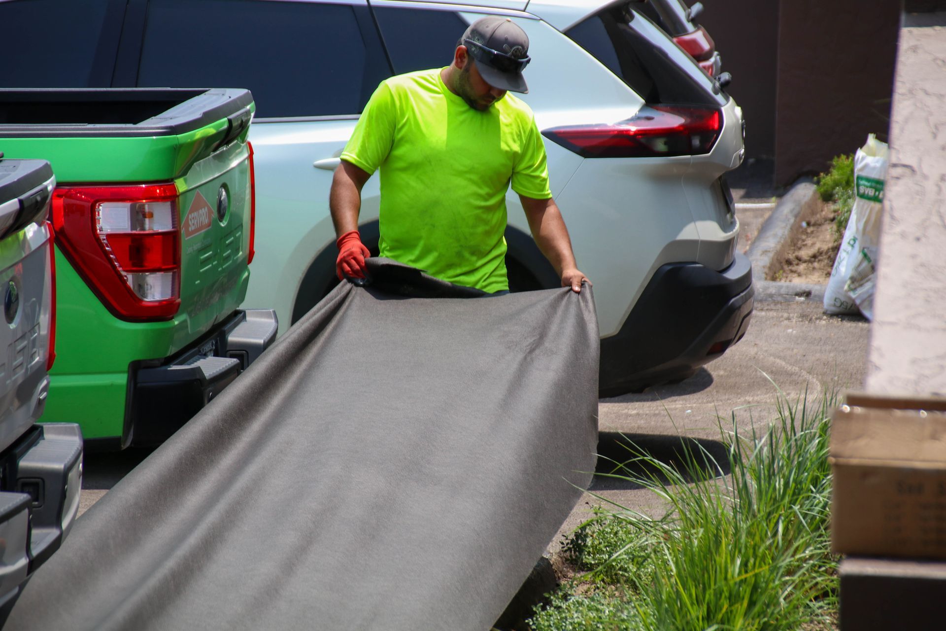 A person in a neon green shirt is unrolling a dark tarp next to a green pickup truck and a white SUV.