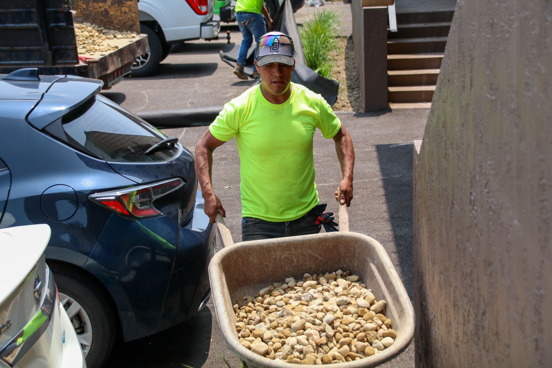 A worker in a neon green shirt pushes a wheelbarrow filled with gravel.