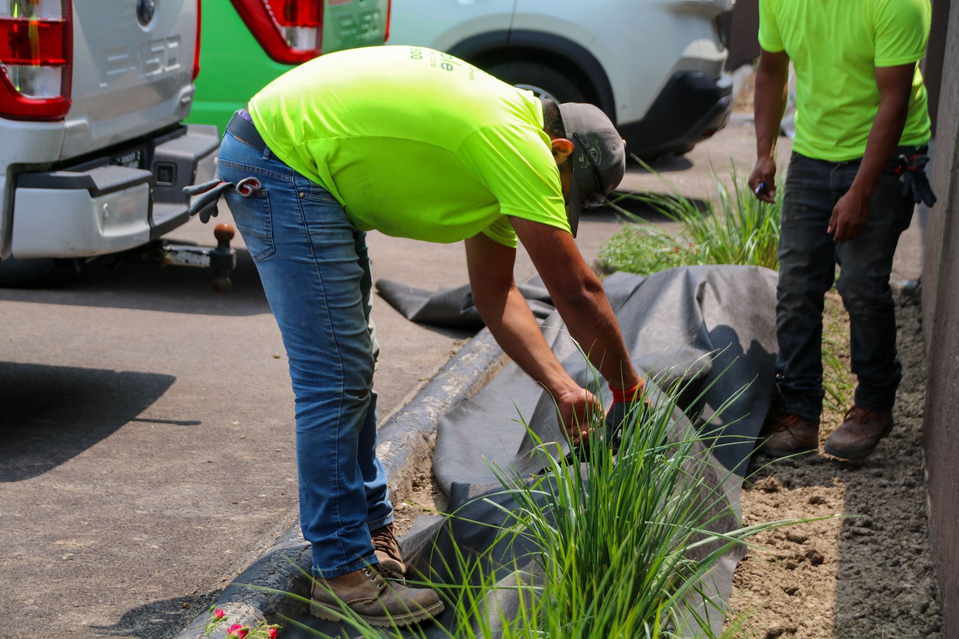 Two workers in neon green shirts installing landscaping in front of a white truck.