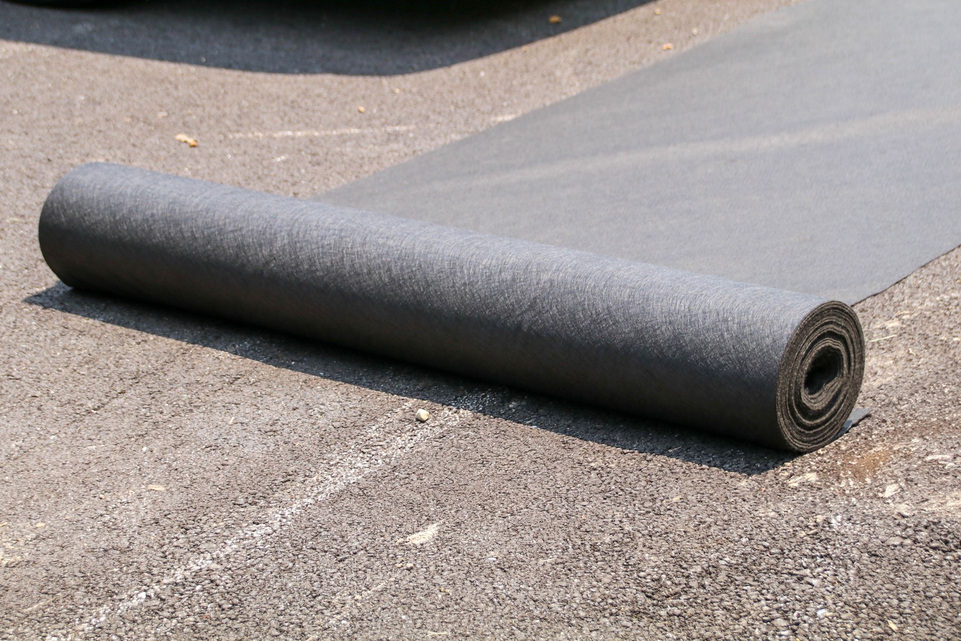 A rolled-up black carpet on a paved surface.