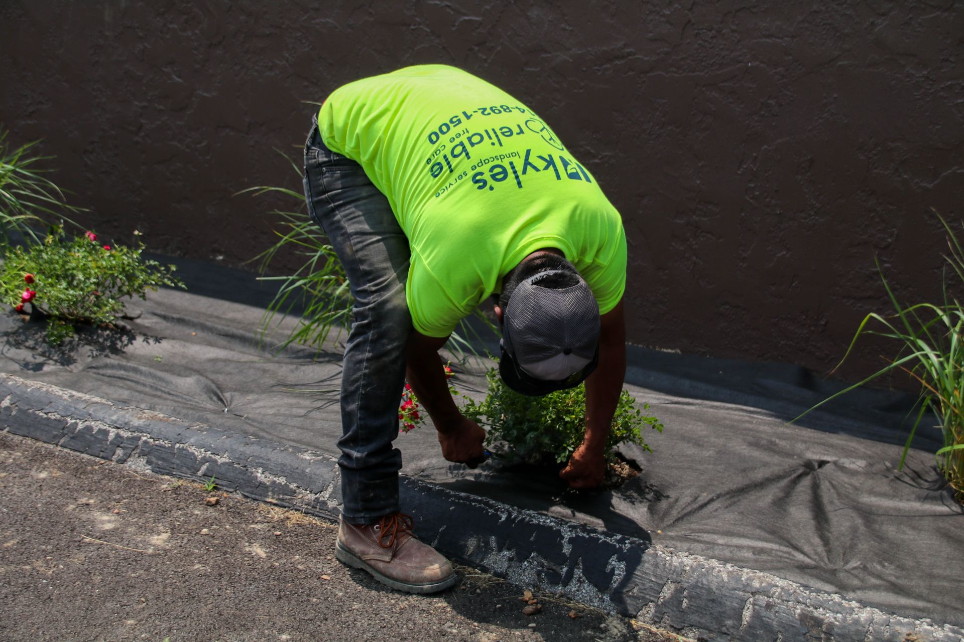 Man in neon green shirt planting flowers next to curb.