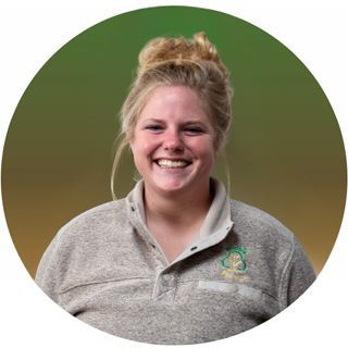 Woman with blonde hair in a bun smiling, wearing a grey sweater, in front of a green and yellow gradient.