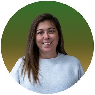 Woman with long brown hair smiling in front of a green and yellow gradient background, wearing a light blue sweater.