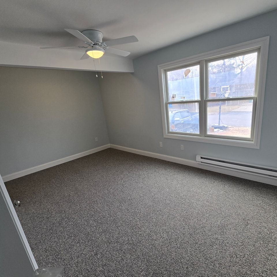 An empty room with a ceiling fan and two windows.