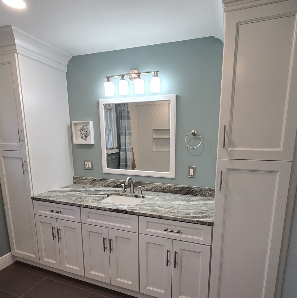 A bathroom with white cabinets a sink and a mirror