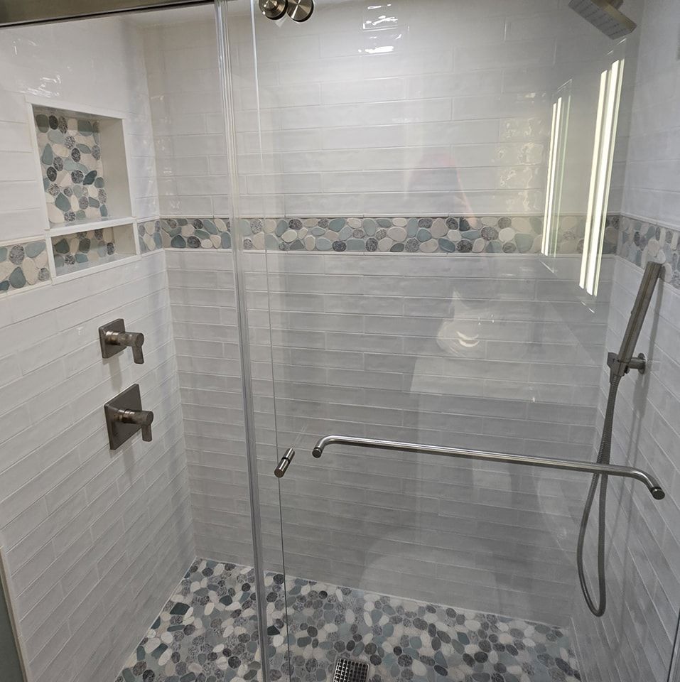 A shower with a glass door and a mosaic floor.