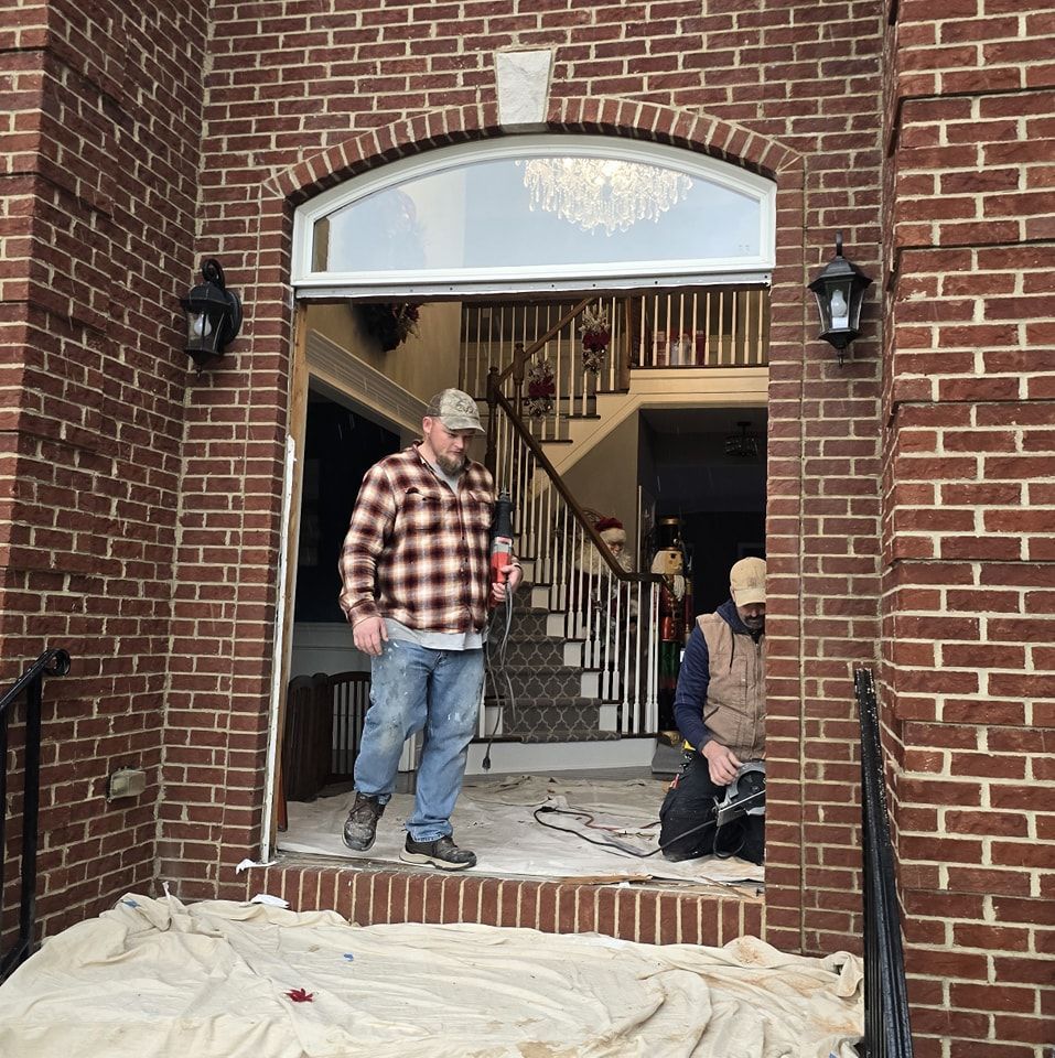 A man in a plaid shirt is standing in front of a brick building