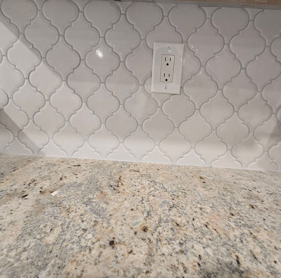 A kitchen counter with a white tile wall and a granite counter top.