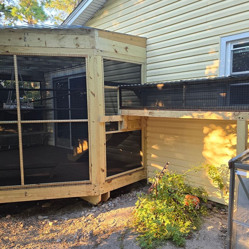 A wooden chicken coop is sitting next to a yellow house.