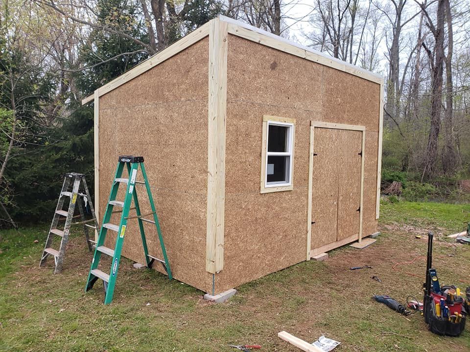 A shed is being built in a backyard with a ladder and a window.