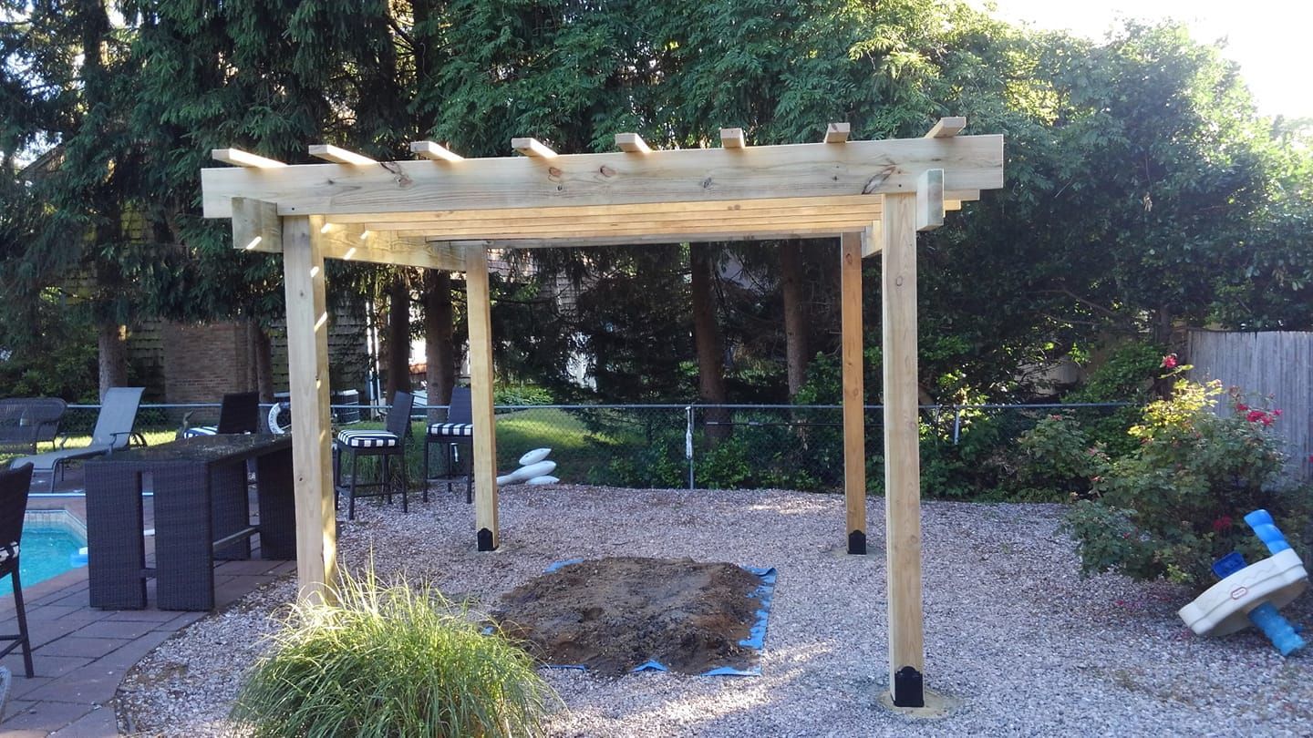 A wooden pergola is sitting on top of a pile of gravel in a backyard.