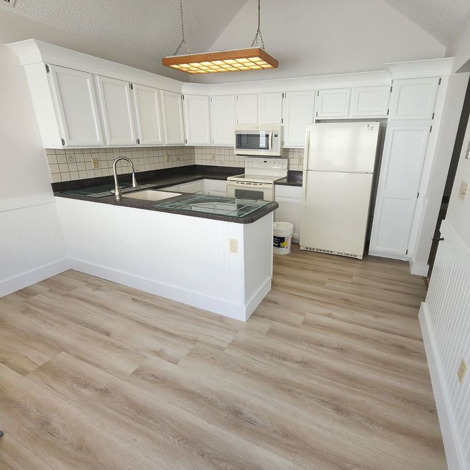 A kitchen with white cabinets , granite counter tops , a refrigerator and a microwave.