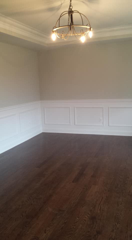 An empty dining room with hardwood floors and a chandelier hanging from the ceiling.