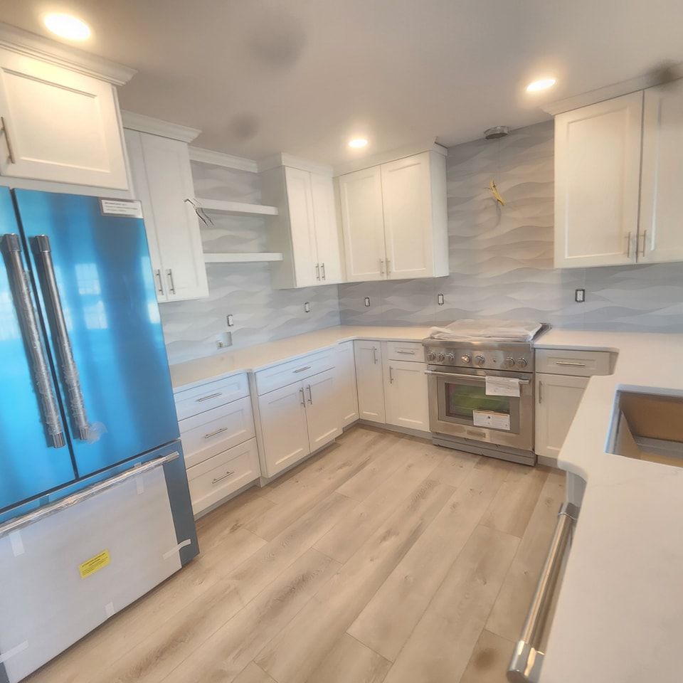 A kitchen with white cabinets , a blue refrigerator , a stove , and a sink.