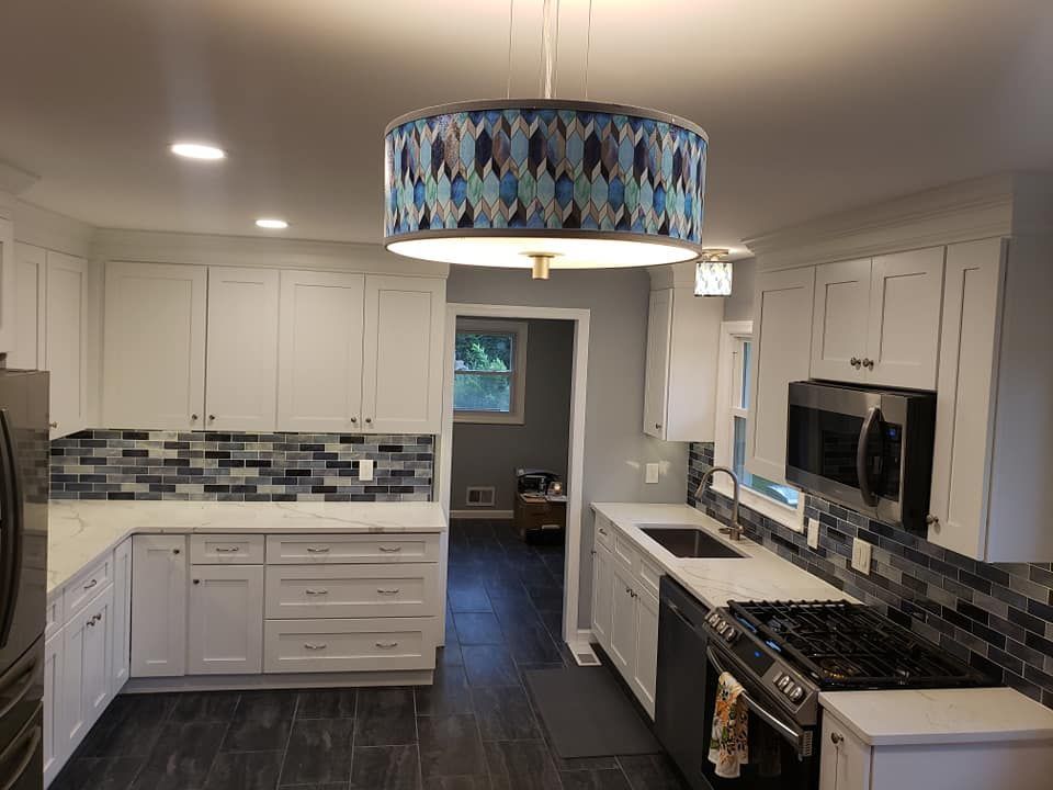 A kitchen with white cabinets , stainless steel appliances , a stove , sink , and a chandelier.