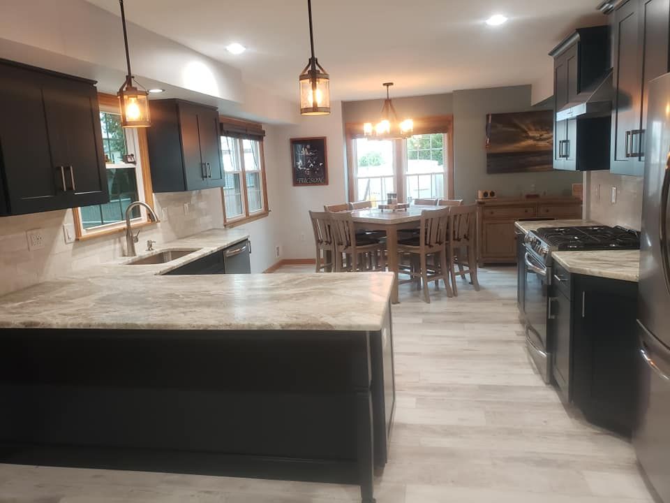 A kitchen with black cabinets and granite counter tops and a dining room in the background.