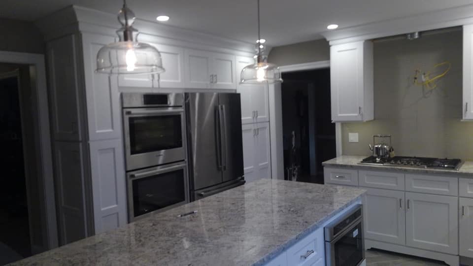A kitchen with white cabinets , stainless steel appliances , granite counter tops and a large island.