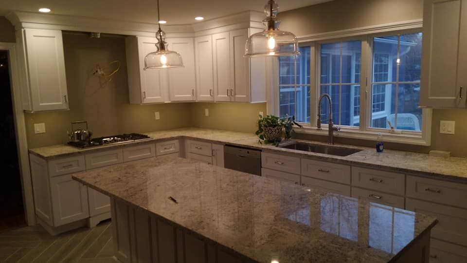A kitchen with white cabinets , granite counter tops , a sink , and a large island.
