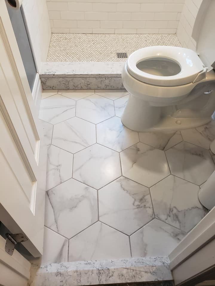 A bathroom with a toilet , shower , and hexagonal tile floor.