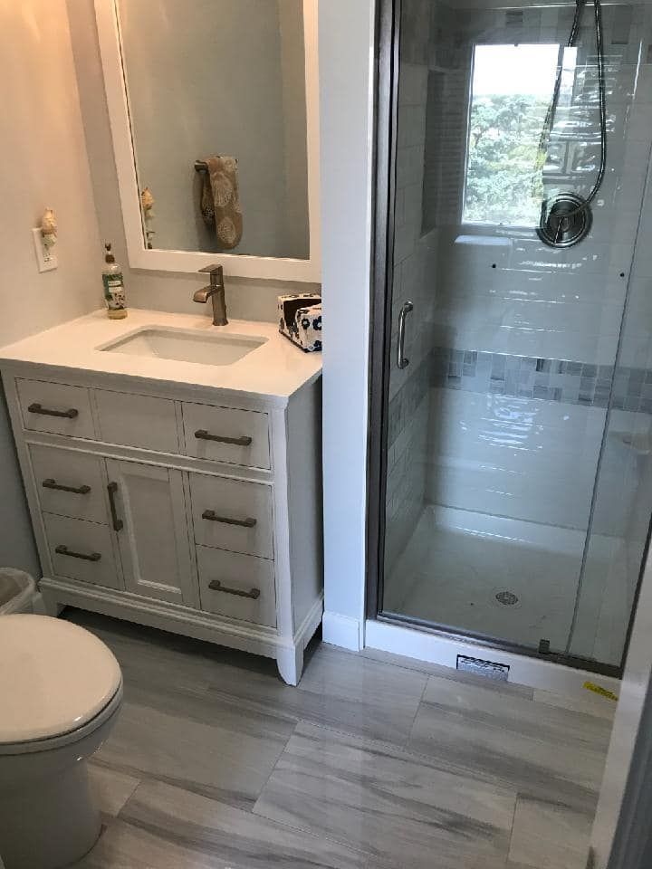 A bathroom with a toilet , sink , mirror and shower.