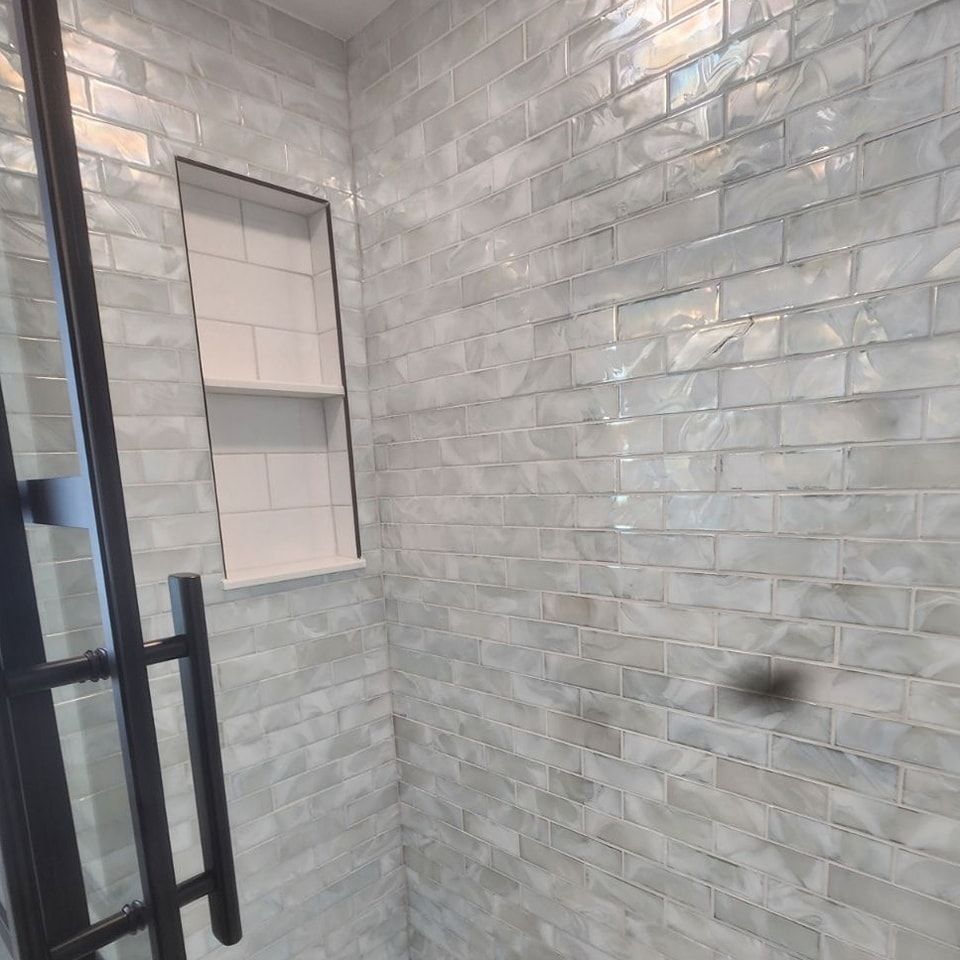 A bathroom with white brick walls and a black shower door.