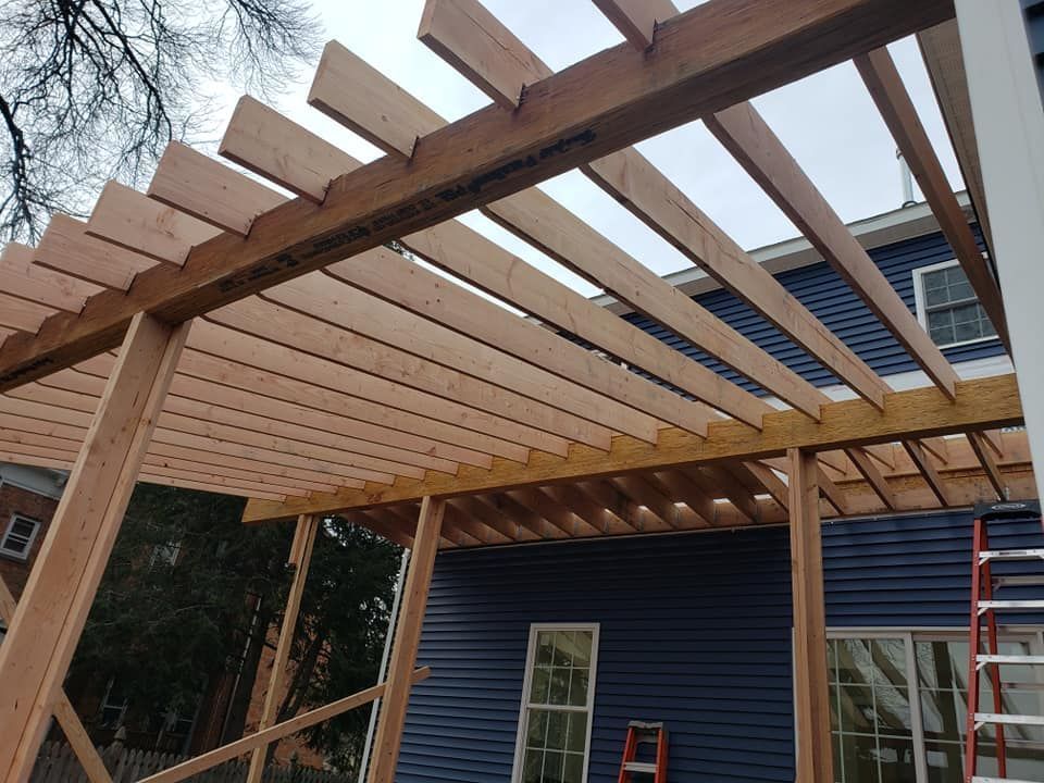 A wooden pergola is being built on the side of a house.