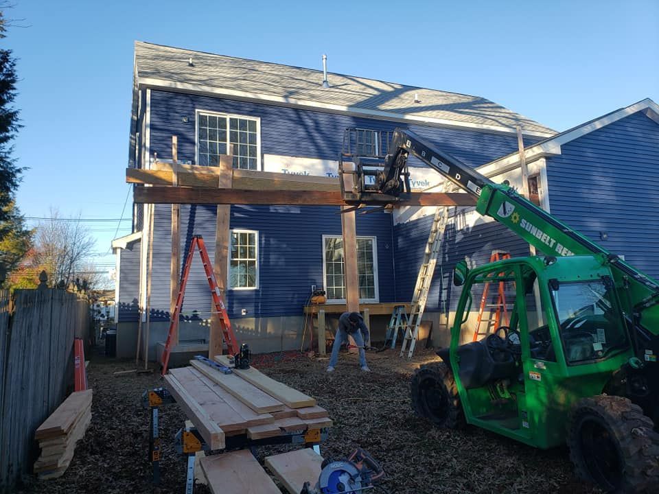 A green forklift is parked in front of a blue house under construction.