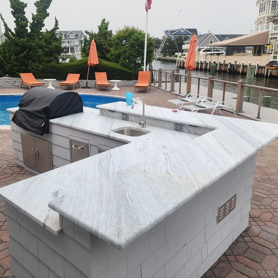 An outdoor kitchen with a grill and a sink in front of a pool