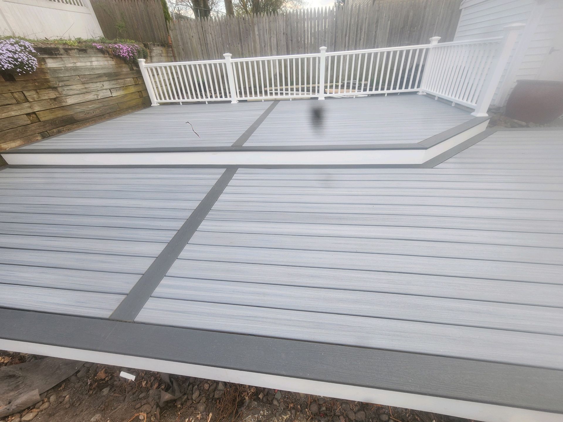 A gray deck with a white railing and a white fence.