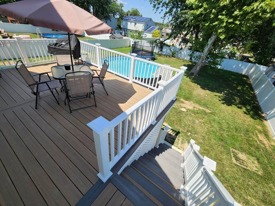A deck with a table and chairs and an umbrella next to a pool.