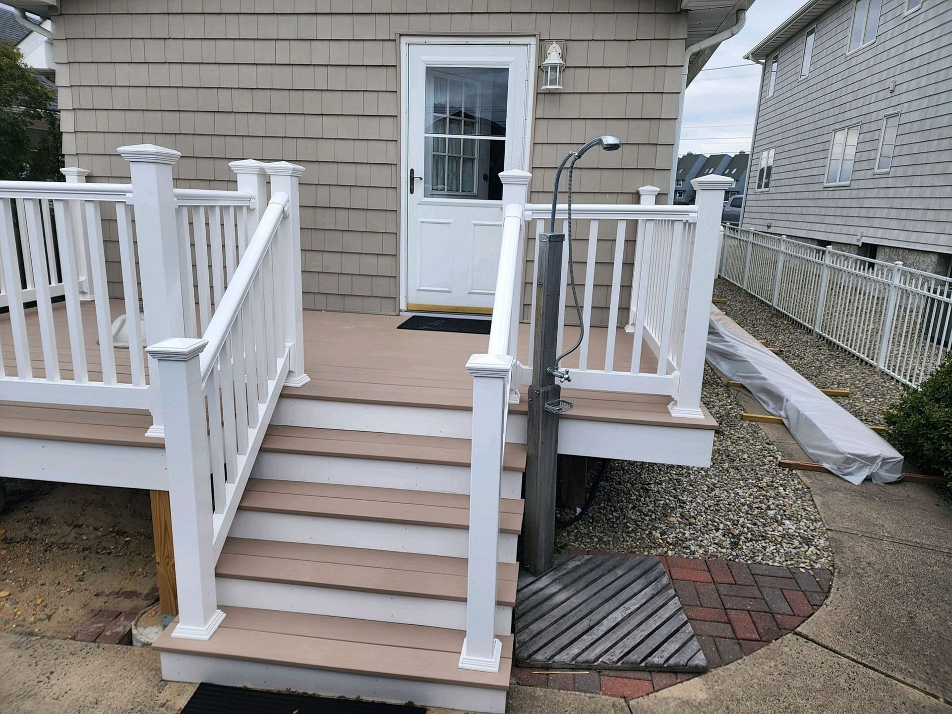 A white deck with stairs and a shower on the side of the house.